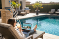 Person watching an online pool care video course on a laptop by a sparkling backyard pool
