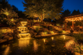 Illuminated backyard water feature at night with glowing underwater LED lights and ambient garden lighting