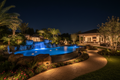 Luxury backyard at night with professionally designed landscape lighting on waterfalls, pool, and garden beds